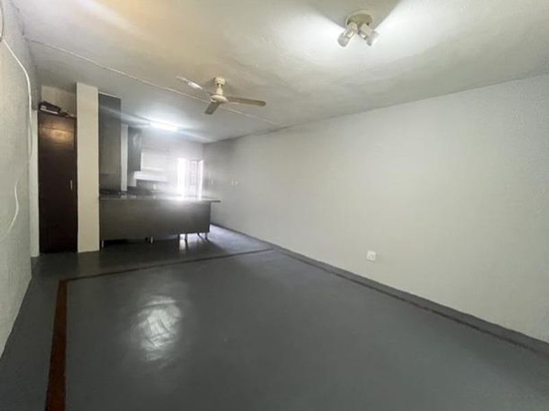 An empty open-plan living and kitchen area featuring a central island, ceiling fan, and basic built-in cabinetry, ready for renovation or staging.