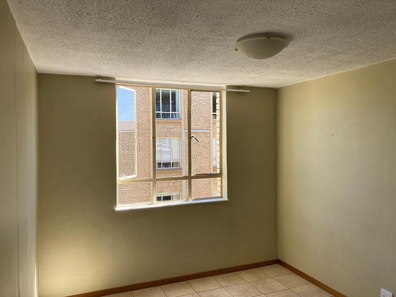 An empty bedroom featuring tiled flooring, a popcorn ceiling, and a large window providing natural light and an urban outlook.