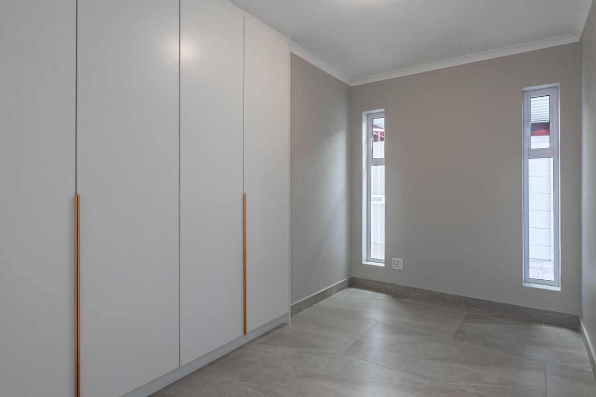 A bright, modern bedroom featuring neutral wall tones, large built-in wardrobes with sleek handles, and contemporary tiled flooring.