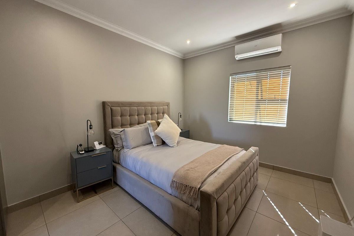 A well-maintained bedroom featuring neutral wall tones, tiled flooring, recessed ceiling lighting, and a wall-mounted air conditioning unit.