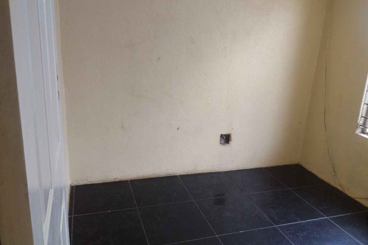 A small, empty room featuring dark floor tiles and plain walls, currently requiring minor cosmetic repairs and finishing touches.