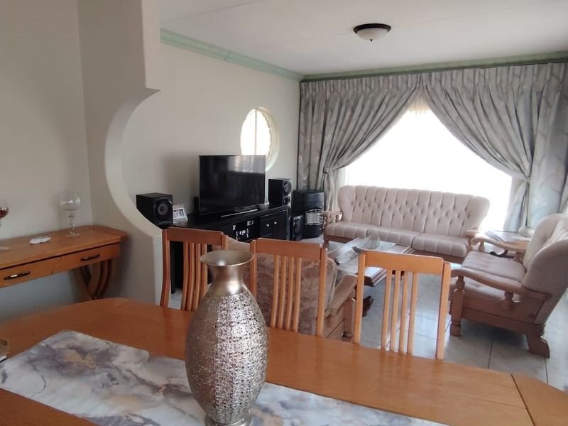 Open plan living and dining area featuring a distinctive architectural archway, porthole window, and tiled flooring, offering a functional and connected living space.