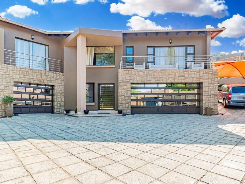 Modern double-story residence featuring stone cladding, a spacious paved driveway, integrated double garages, and upper-level balconies.