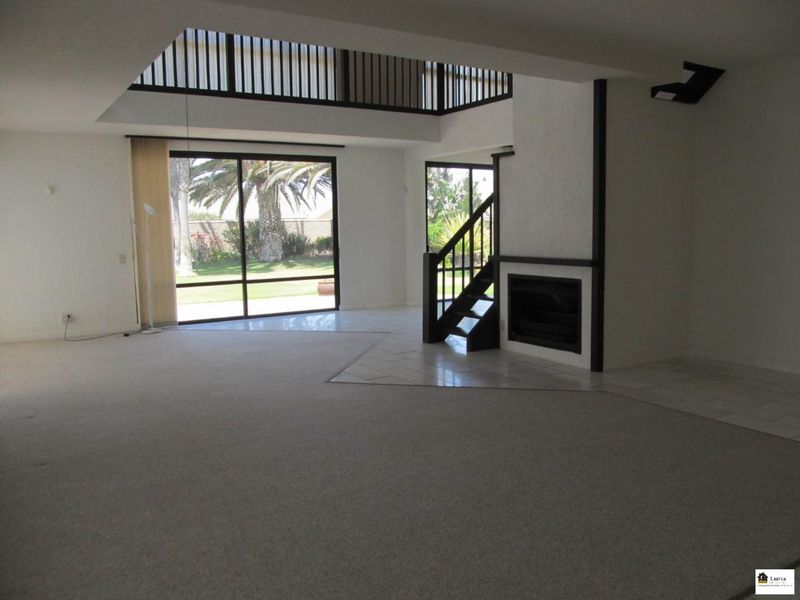 Spacious open-plan living area featuring a fireplace, staircase, mezzanine level, and large sliding glass doors providing access to the garden.