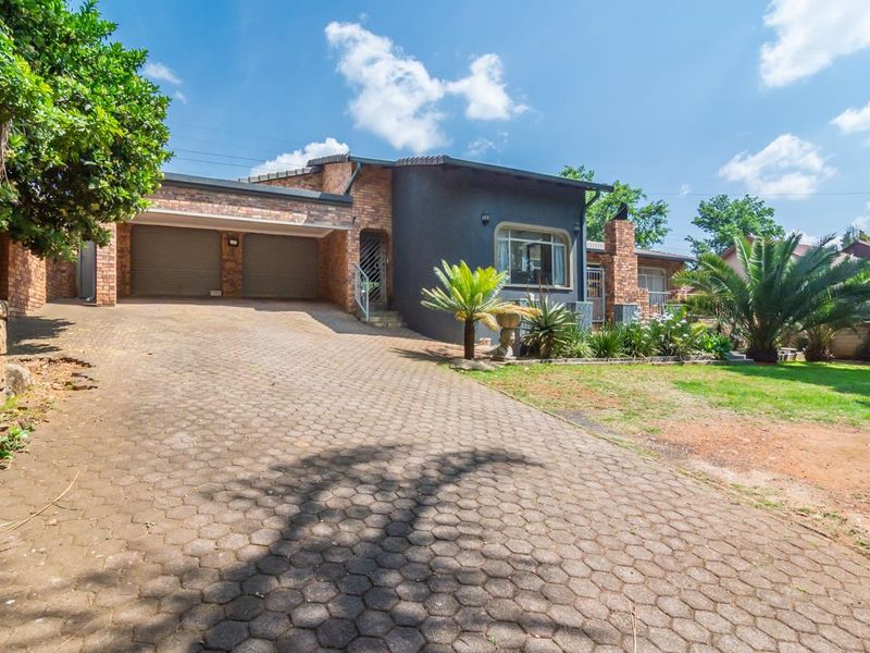 Front exterior view of a house featuring a double garage, paved driveway, and established garden area.
