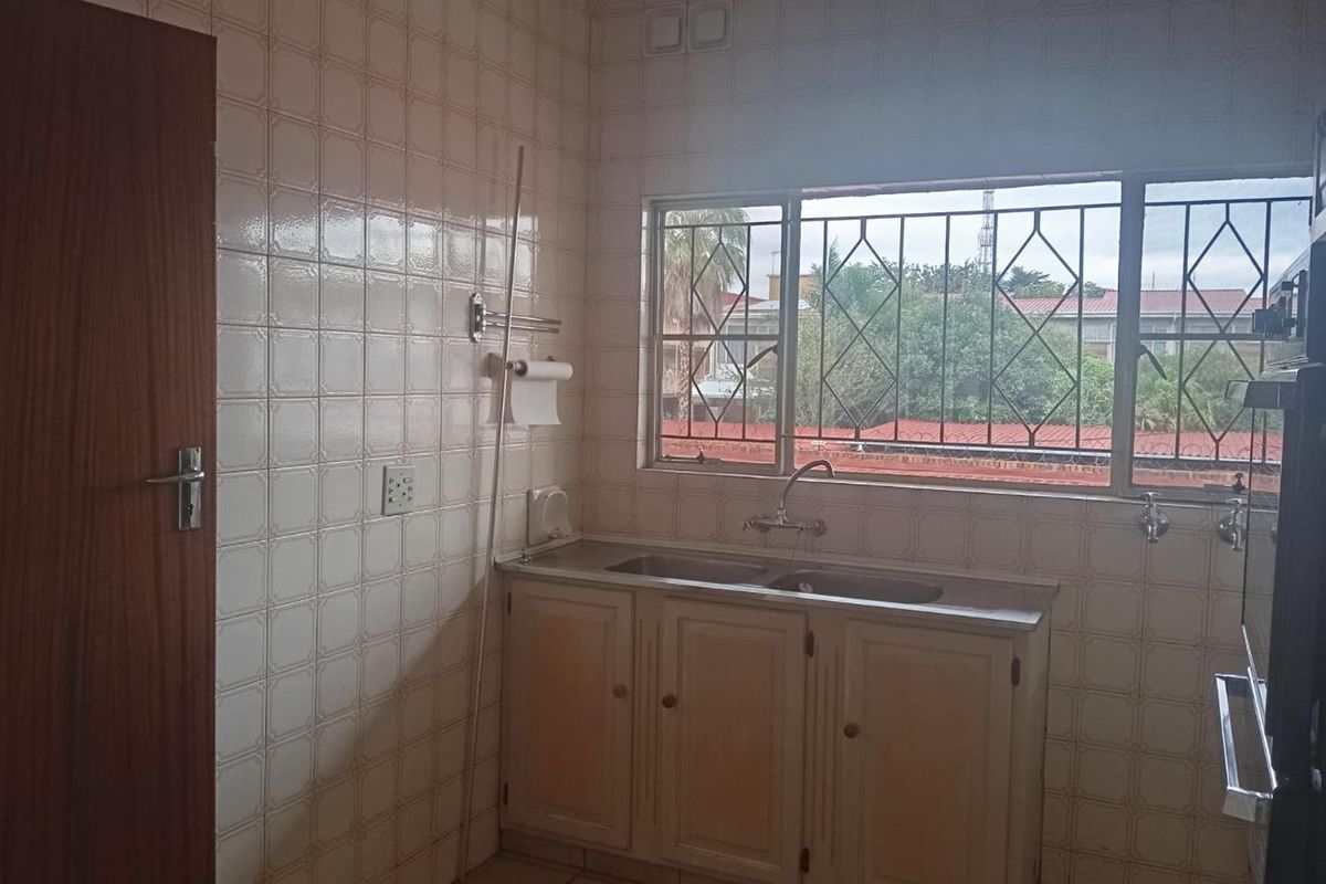 A dated kitchen area featuring tiled walls, a double basin sink with built-in cabinetry, and a window with security bars.