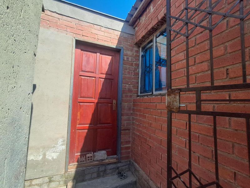 Exterior view of a rear entrance featuring exposed brick walls, a timber door, and a metal security gate with visible signs of wear.