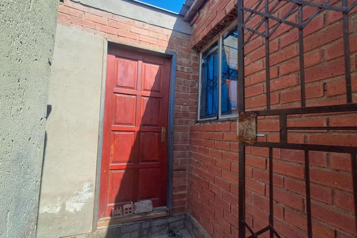 Exterior view of a rear entrance featuring exposed brick walls, a timber door, and a metal security gate with visible signs of wear.