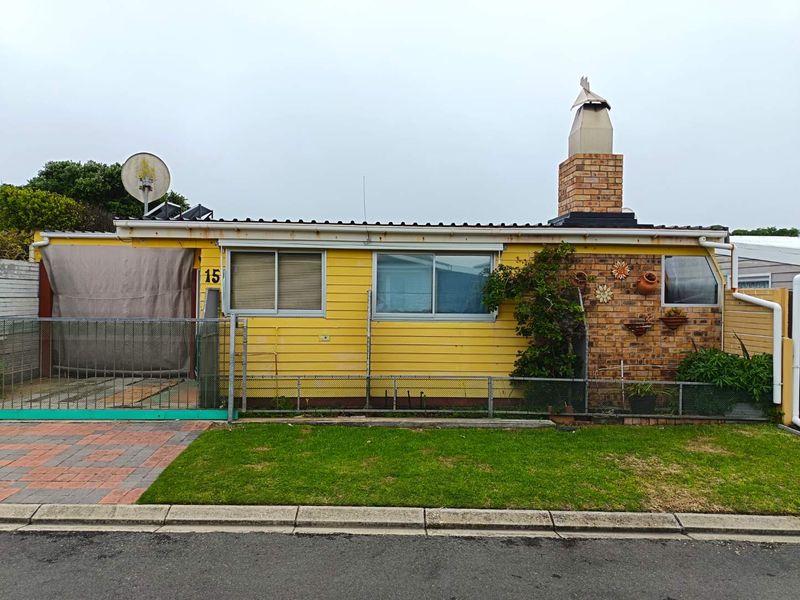 Front elevation of a single-story yellow house featuring a brick chimney, sliding windows, and a small front lawn with a paved driveway.
