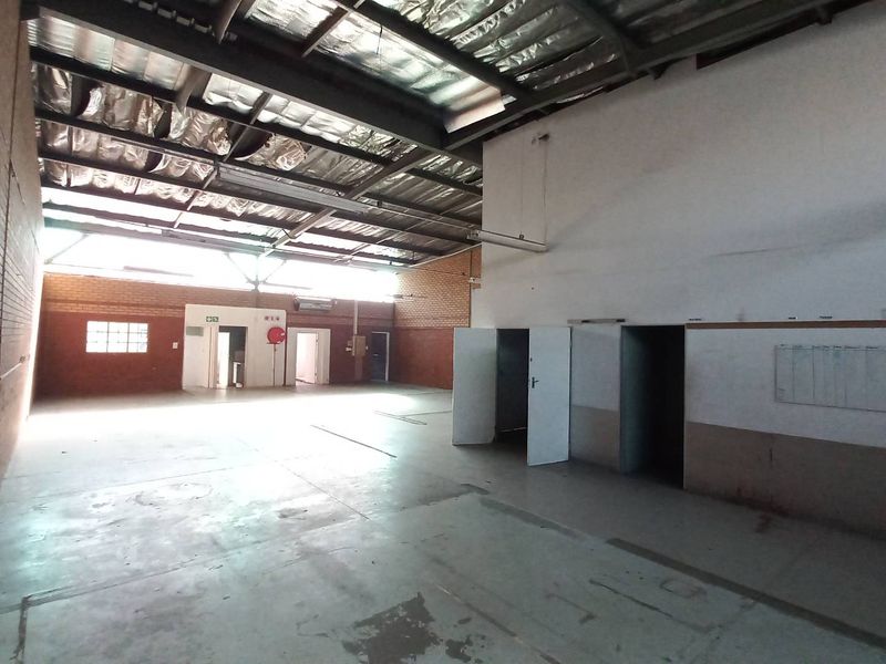 Spacious industrial warehouse area featuring high exposed ceilings, brick wall finishes, and multiple access points, suitable for storage or manufacturing operations.