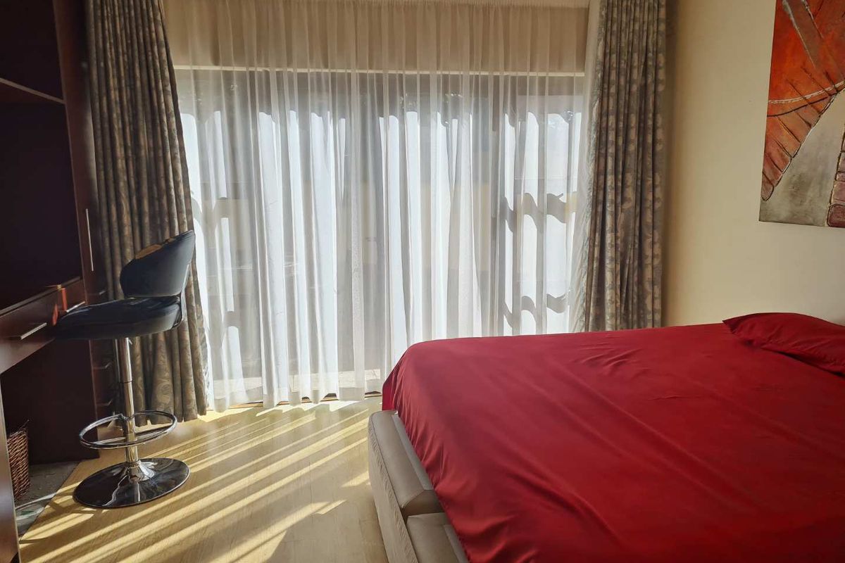 A well-lit bedroom featuring laminate flooring and large sliding glass doors with curtains, providing direct access to the exterior.