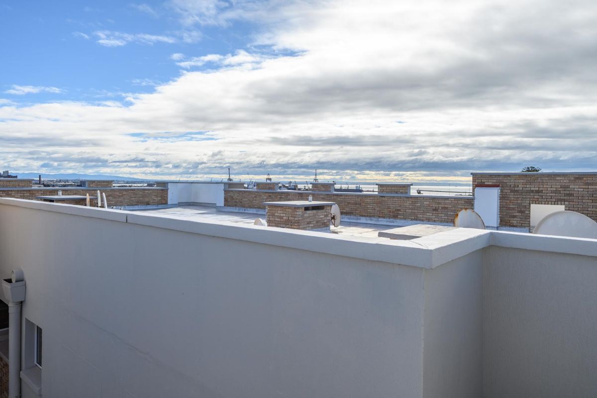 An elevated view of a flat roof terrace featuring brick parapet walls and distant coastal views.
