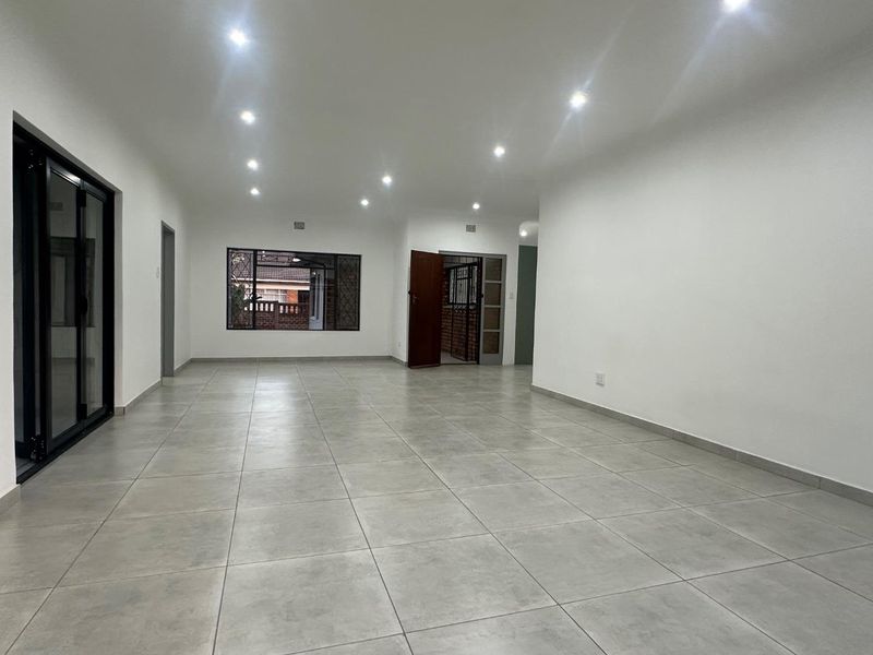 Spacious, open-plan living area featuring neutral ceramic floor tiles, recessed downlighting, and access to outdoor space through a modern sliding glass door.