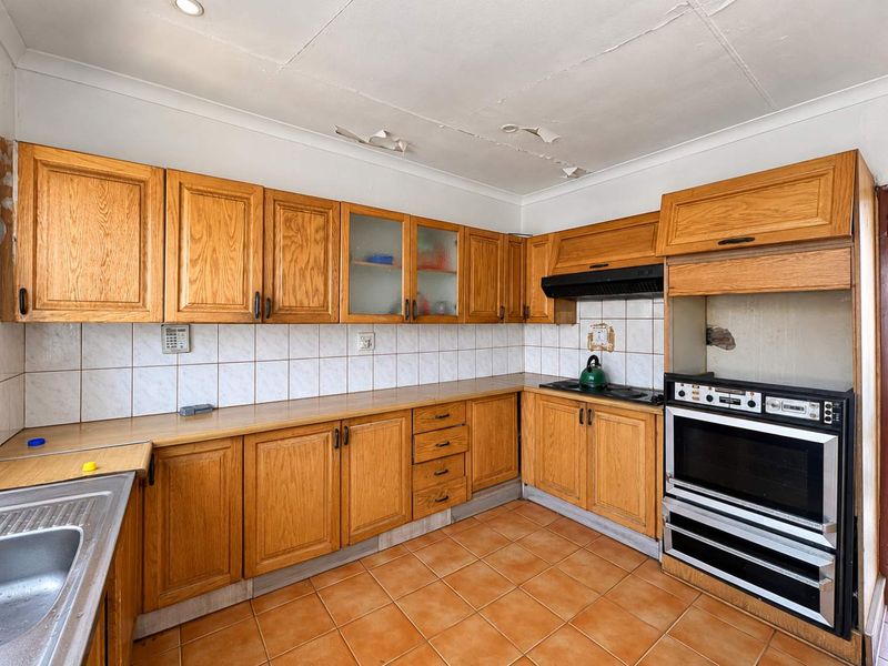 A dated kitchen featuring wooden cabinetry, tiled backsplash, and built-in appliances, requiring ceiling repairs and cosmetic updates to modernize the space.