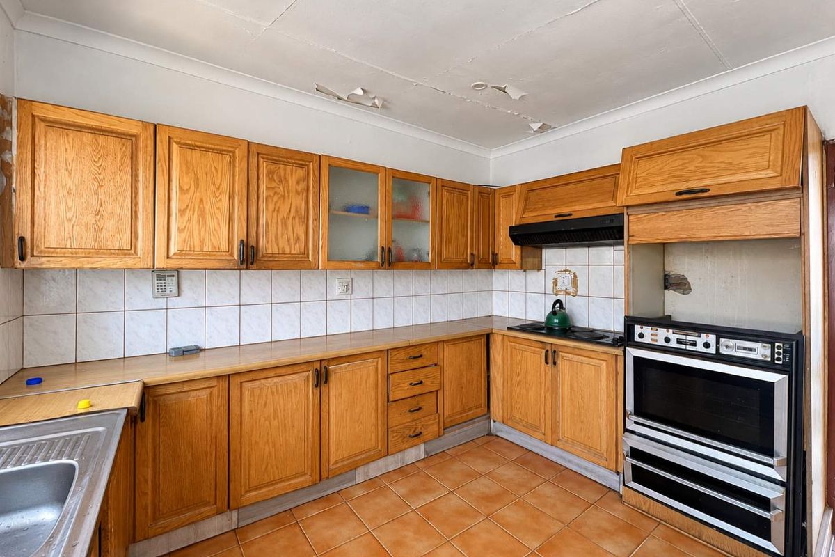 A dated kitchen featuring wooden cabinetry, tiled backsplash, and built-in appliances, requiring ceiling repairs and cosmetic updates to modernize the space.