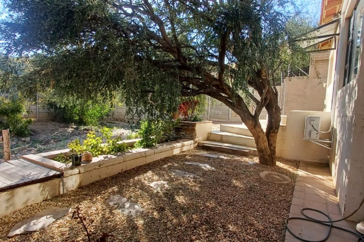 Rear garden area featuring a mature tree, gravel landscaping, raised stone garden beds, and concrete steps leading to the property exterior.