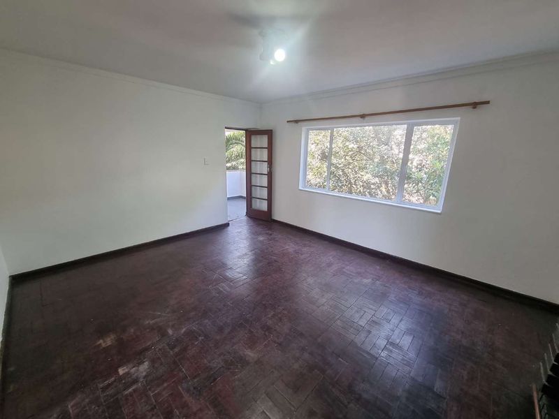 Spacious living room featuring original parquet flooring, large windows for natural light, and direct access to an outdoor area through a timber-framed glass door.
