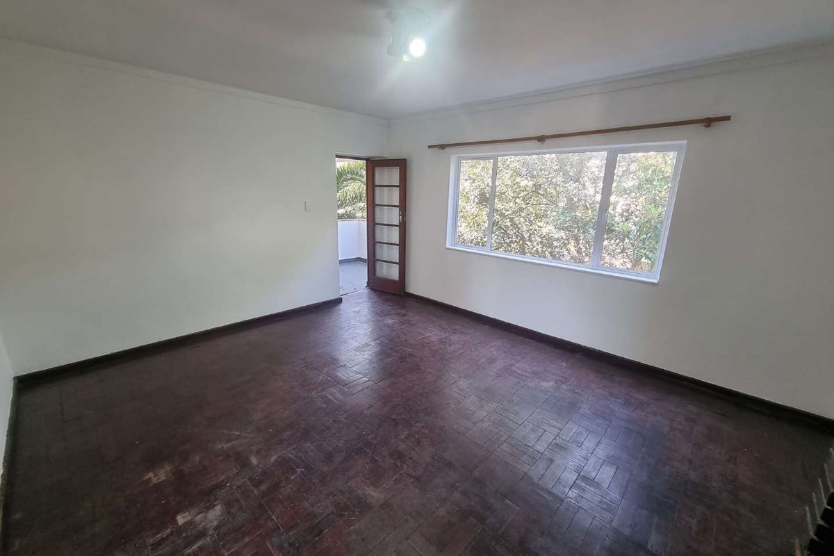 Spacious living room featuring original parquet flooring, large windows for natural light, and direct access to an outdoor area through a timber-framed glass door.