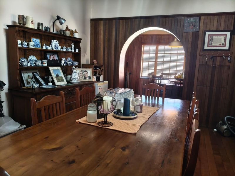 A traditional dining room featuring warm timber wall paneling, polished timber flooring, and a distinctive arched doorway leading to an adjacent space.
