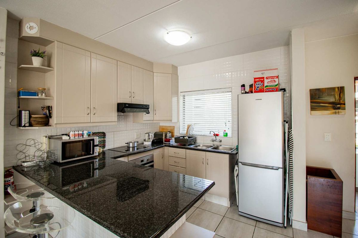 A functional kitchen featuring granite countertops, built-in cabinetry, a stainless steel sink, and integrated appliances including an oven and hob.