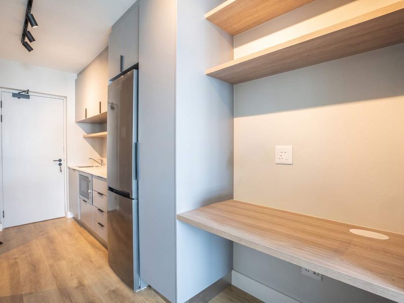 Modern kitchen featuring sleek grey cabinetry, integrated appliances, wood-look laminate flooring, and a convenient built-in desk area with floating shelves.