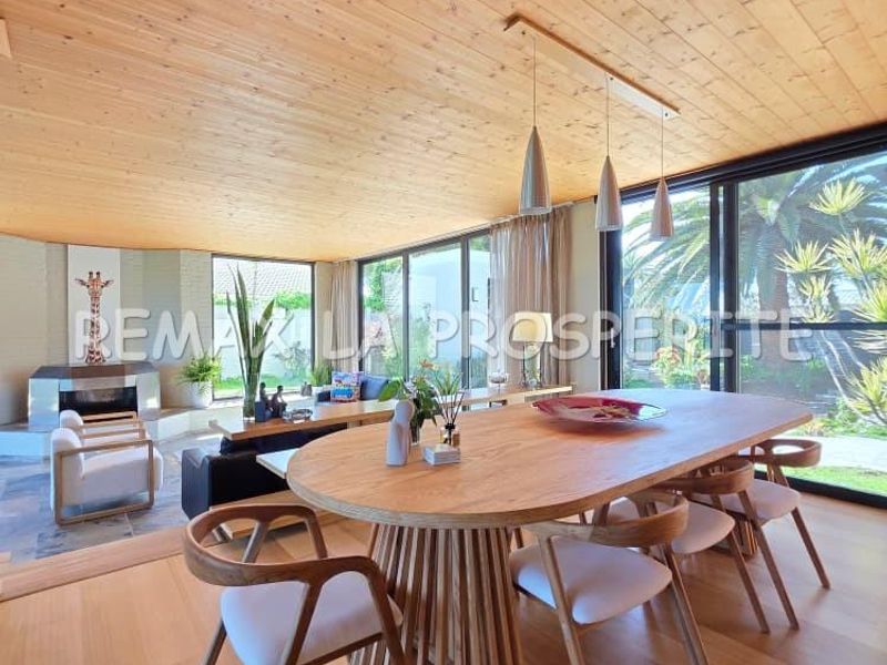 Spacious open-plan living and dining area featuring a warm timber ceiling, fireplace, and expansive sliding glass doors that provide seamless indoor-outdoor flow.