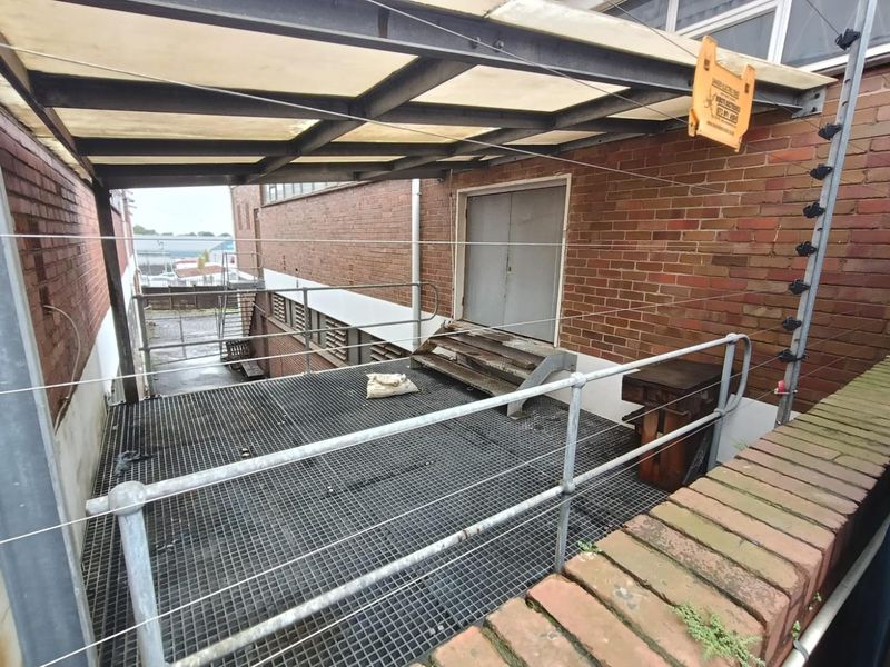 Industrial rear exterior area featuring a metal grating platform, steel safety railings, and a covered walkway with an integrated electric fence.