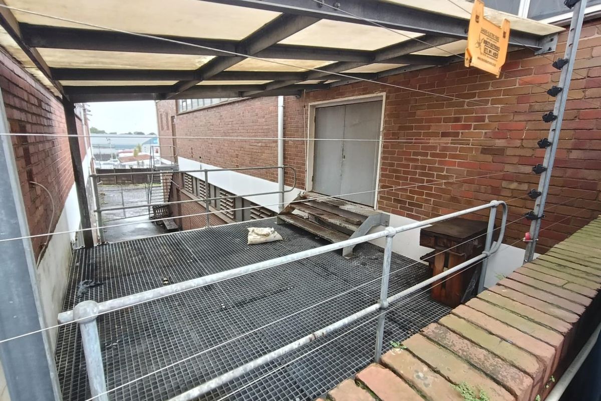 Industrial rear exterior area featuring a metal grating platform, steel safety railings, and a covered walkway with an integrated electric fence.