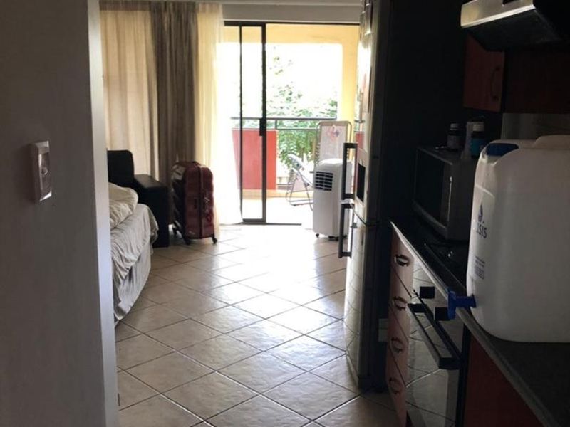 Open-plan apartment layout featuring a compact kitchen with built-in cabinetry and appliances, leading to a living area with access to a balcony.