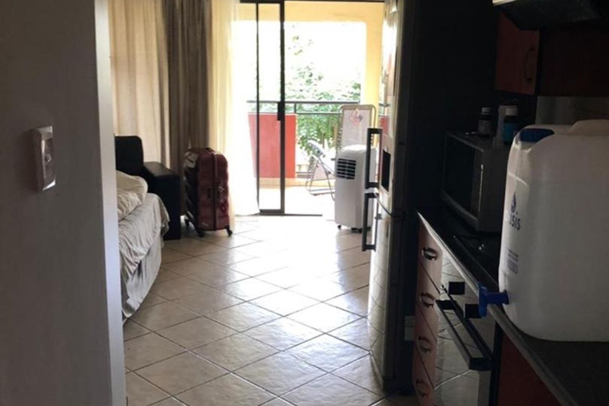 Open-plan apartment layout featuring a compact kitchen with built-in cabinetry and appliances, leading to a living area with access to a balcony.
