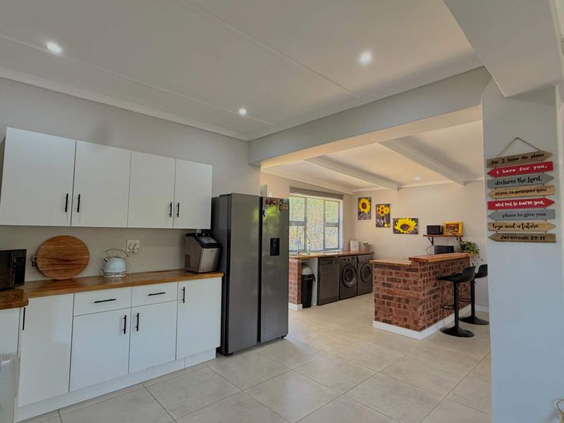 Spacious open-plan kitchen featuring white cabinetry, wooden countertops, and an exposed brick breakfast bar, seamlessly flowing into a functional laundry area.