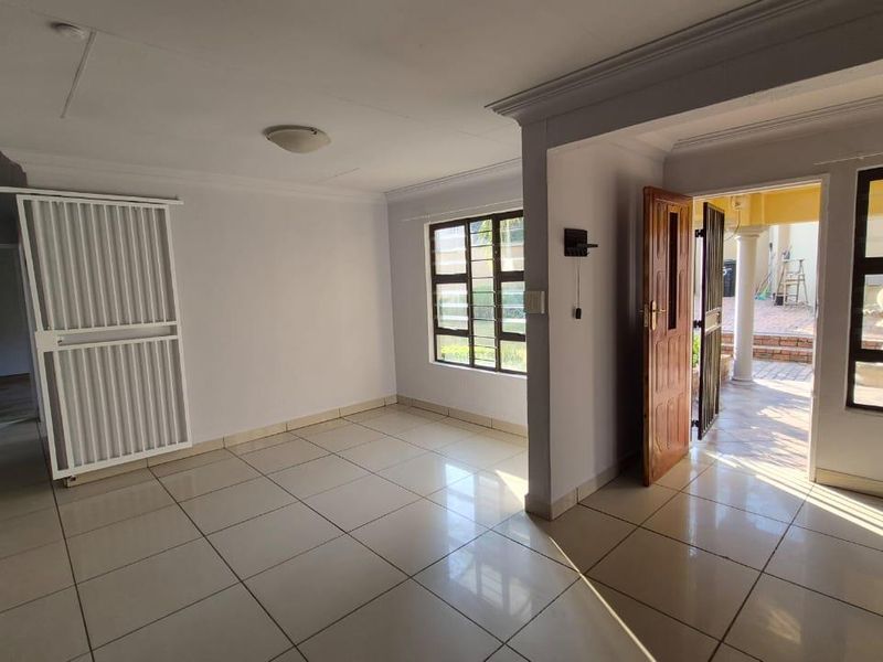 An open-plan living area featuring neutral tiled flooring, cornicing, and direct access to an outdoor patio through a timber entrance door.