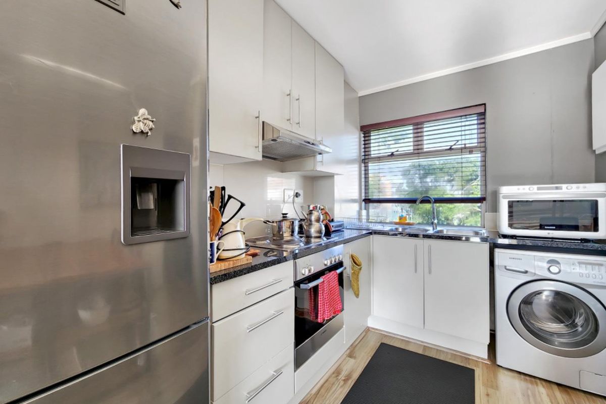 A compact, functional kitchen featuring modern white cabinetry, dark countertops, integrated appliances, and a window providing natural light.