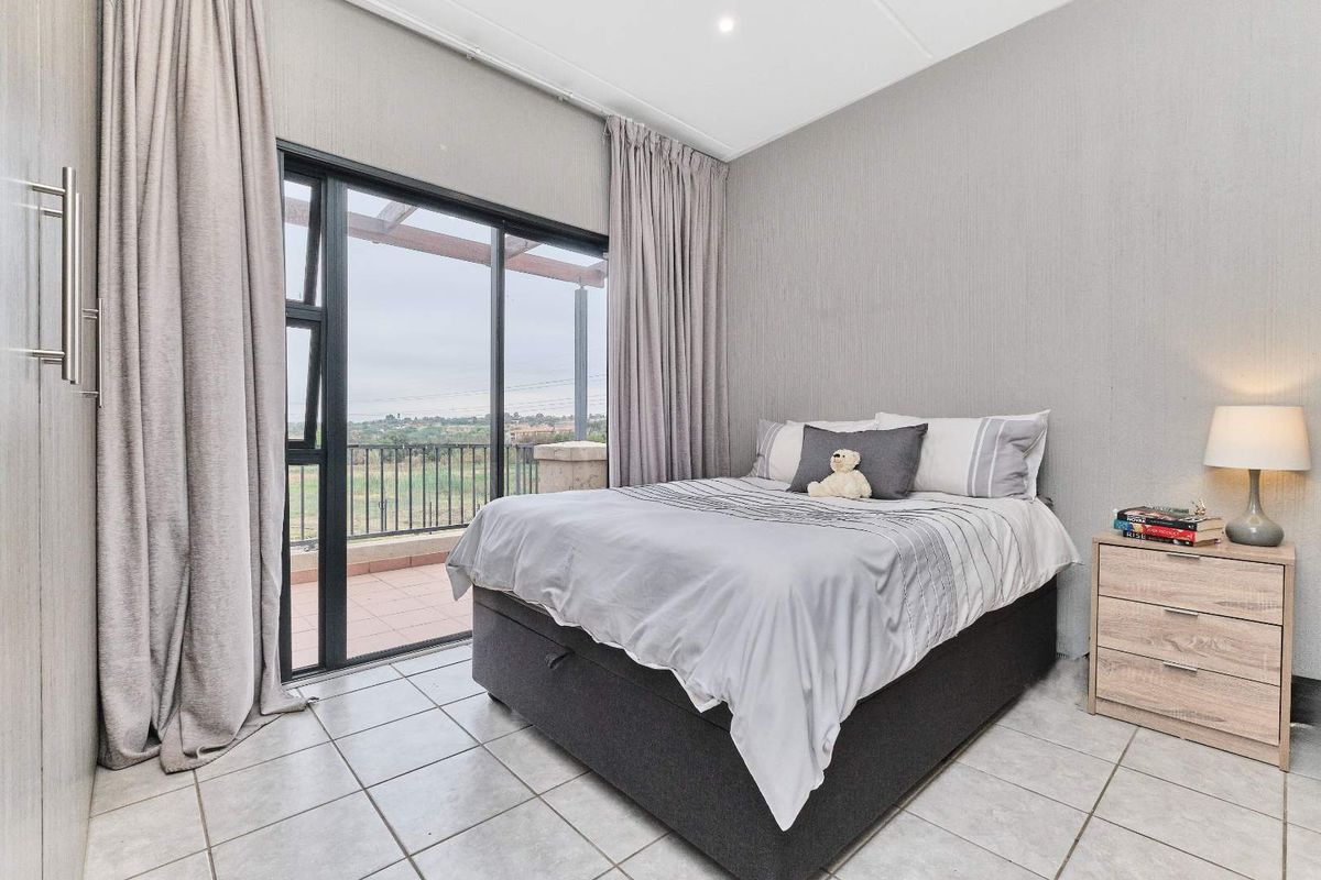 A well-maintained bedroom featuring tiled flooring, built-in cupboards, and large sliding glass doors that open onto a private balcony with scenic views.