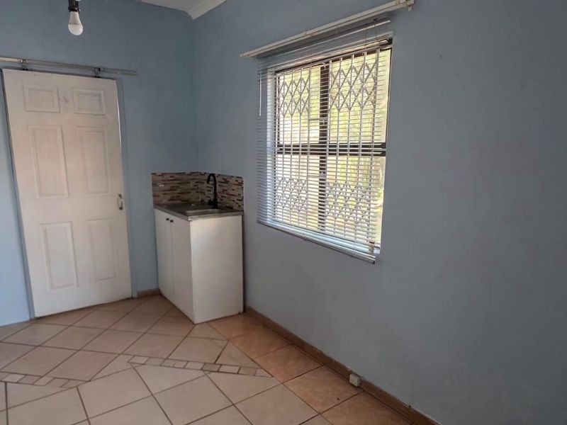 A functional scullery or utility area featuring tiled flooring, built-in cabinetry with a sink, and a window with security bars.