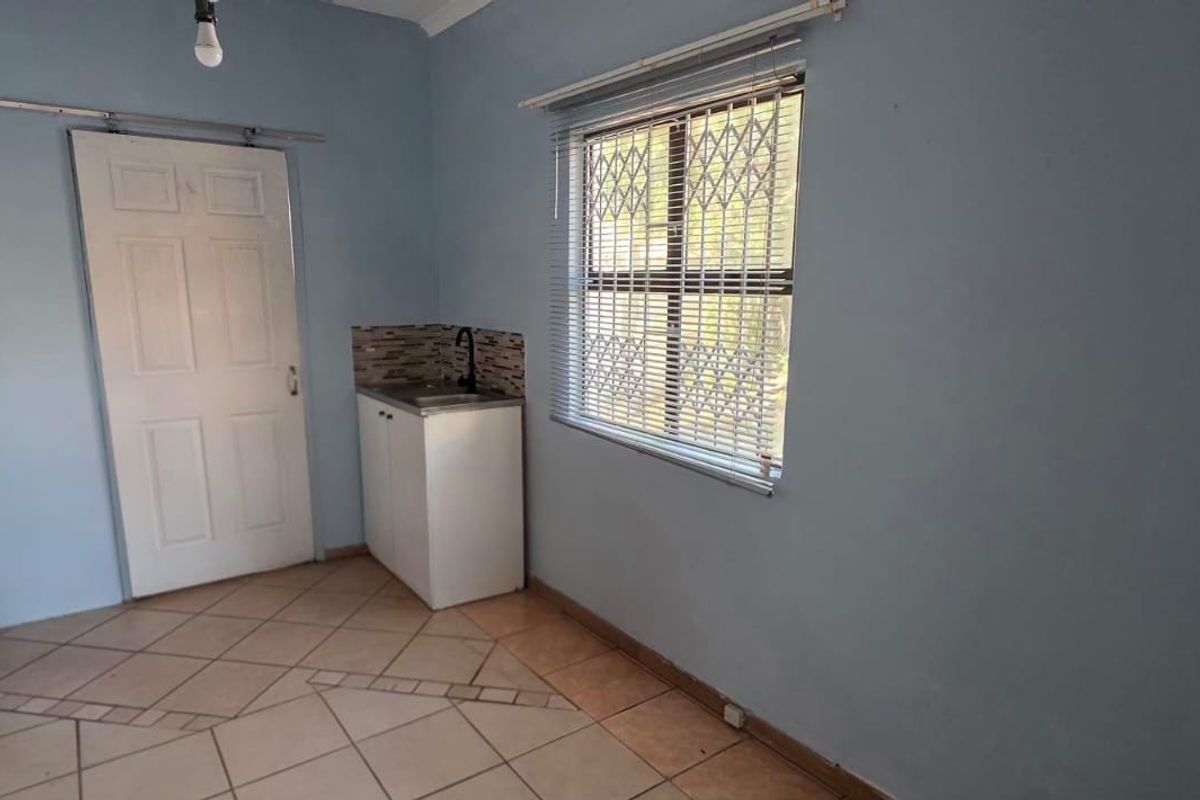 A functional scullery or utility area featuring tiled flooring, built-in cabinetry with a sink, and a window with security bars.