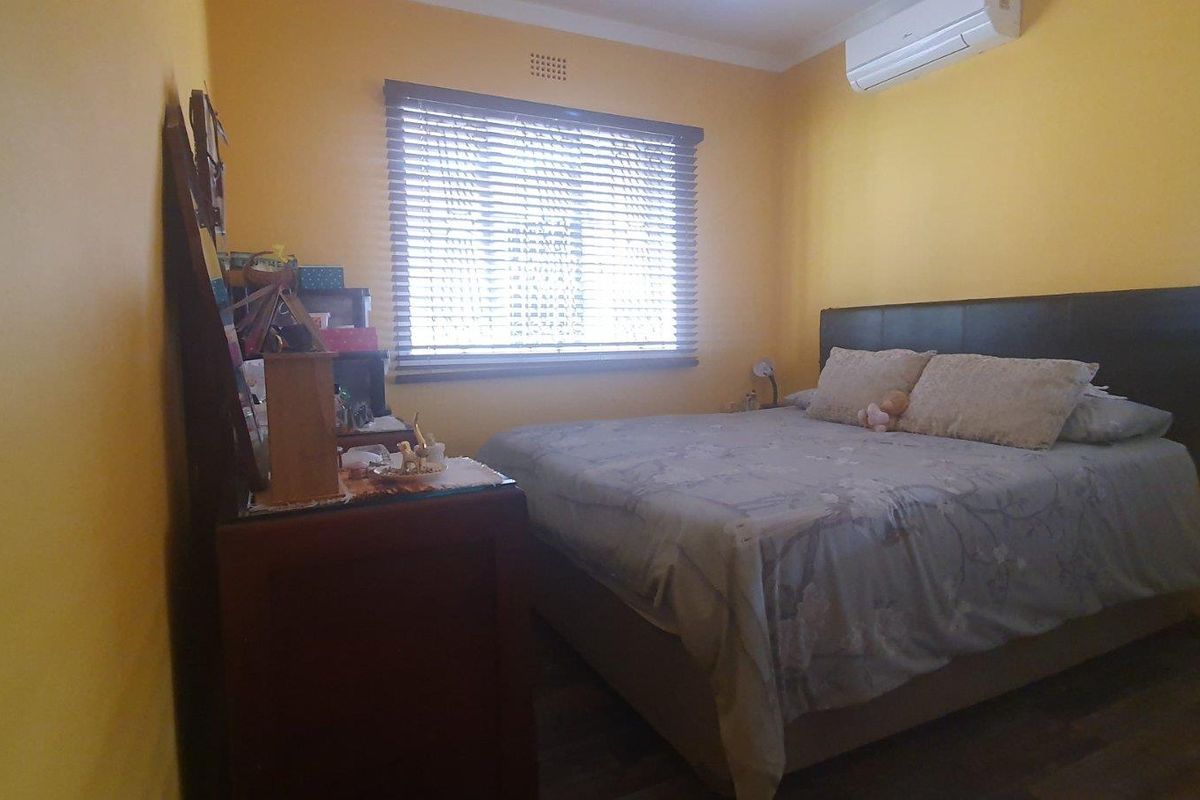 A bedroom featuring laminate flooring, venetian blinds, and a wall-mounted split-system air conditioner.