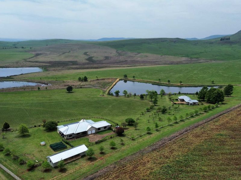 Aerial view of a sprawling farm property featuring a main residence, outbuildings, a private dam, and extensive surrounding pasture land.