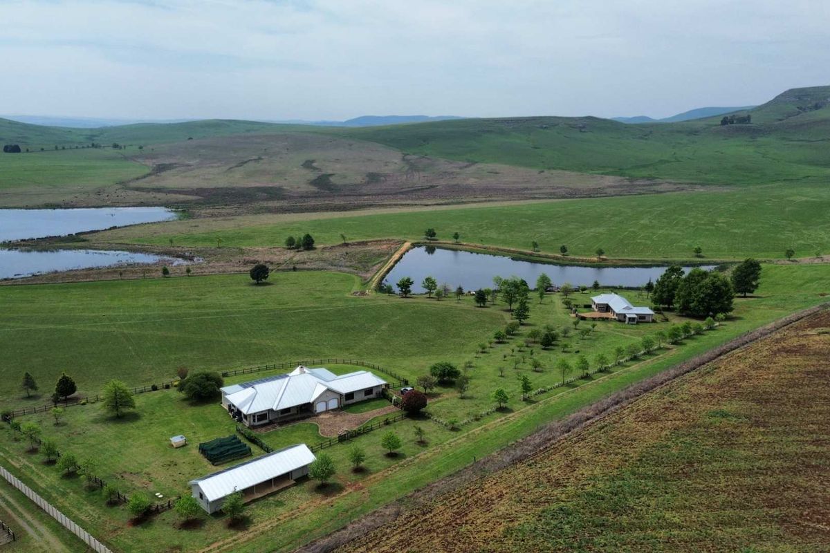 Aerial view of a sprawling farm property featuring a main residence, outbuildings, a private dam, and extensive surrounding pasture land.