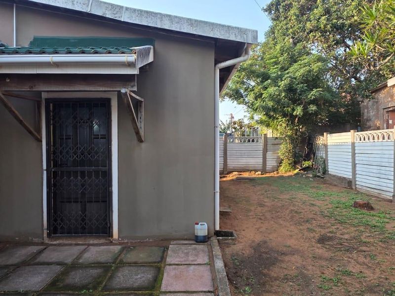 Rear exterior view of the cottage featuring a small paved patio area, security gate, and a fenced garden space with perimeter walling.