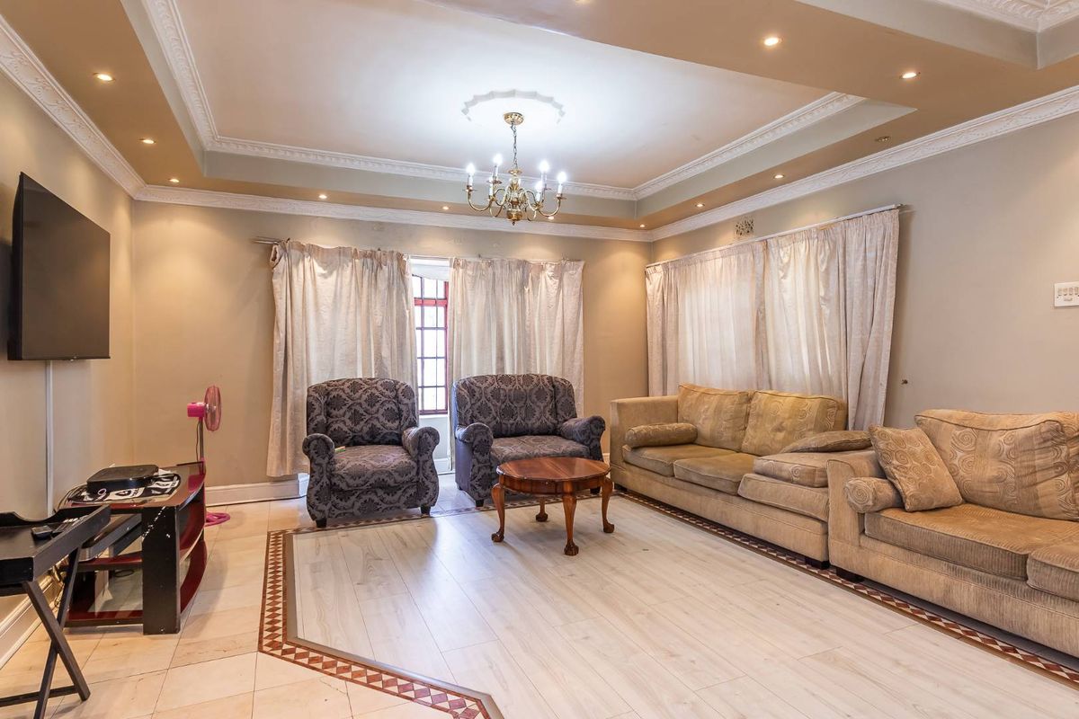 Spacious living room featuring a tray ceiling with recessed lighting, decorative crown molding, and a combination of tiled and wood-look flooring.