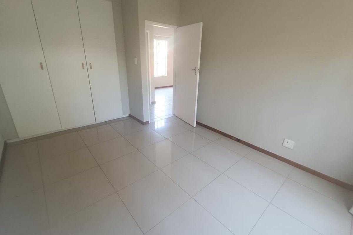 A clean, empty bedroom featuring neutral tiled flooring and built-in cupboards, offering a blank canvas for personalization.