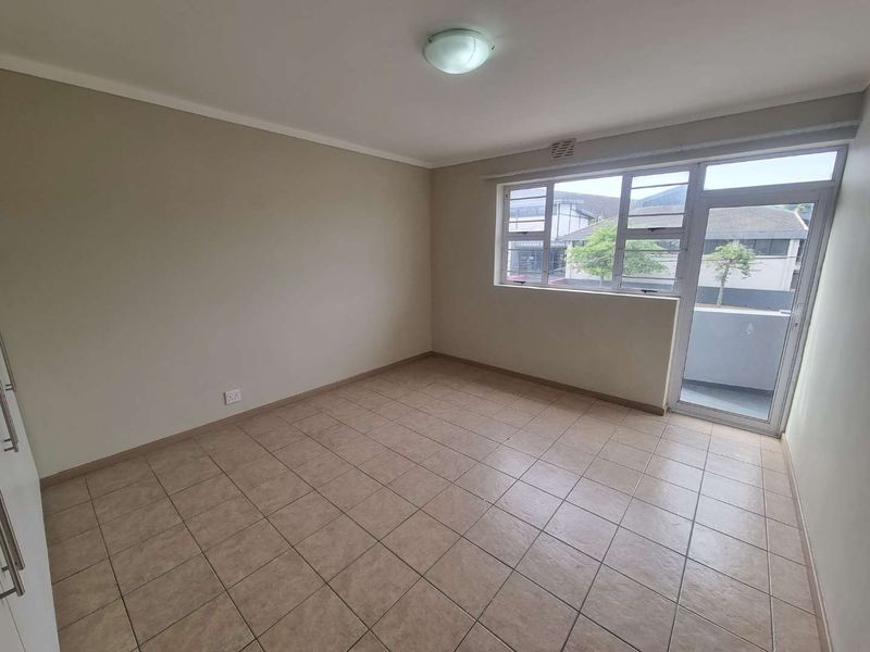 A bright, empty bedroom featuring tiled flooring, built-in cupboards, and direct access to an outdoor balcony through a glass door.