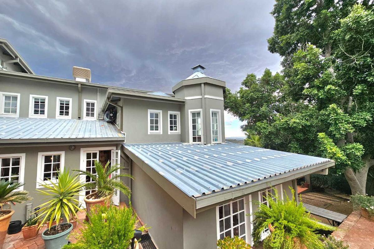 Rear exterior view of the house featuring a corrugated metal roof, multi-pane windows, and a brick-paved patio area surrounded by mature trees.