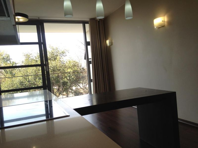Open plan kitchen and living area featuring a built-in island with integrated hob, modern lighting, and large glass sliding doors leading to a balcony.