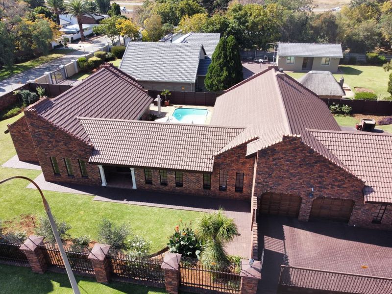 Aerial view of a face brick residential property featuring a tiled roof, swimming pool, double garage, and well-maintained garden with paved driveway.