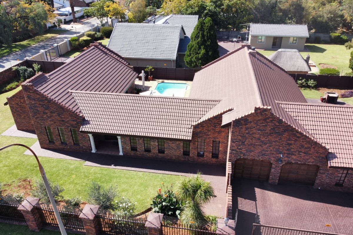 Aerial view of a face brick residential property featuring a tiled roof, swimming pool, double garage, and well-maintained garden with paved driveway.