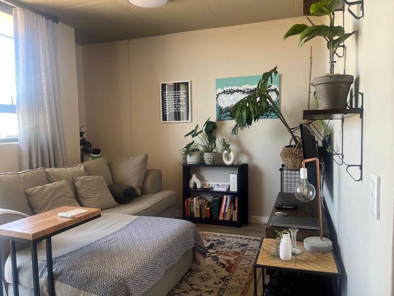A cozy living room area featuring neutral wall tones, a large window with curtains, and functional electrical points.