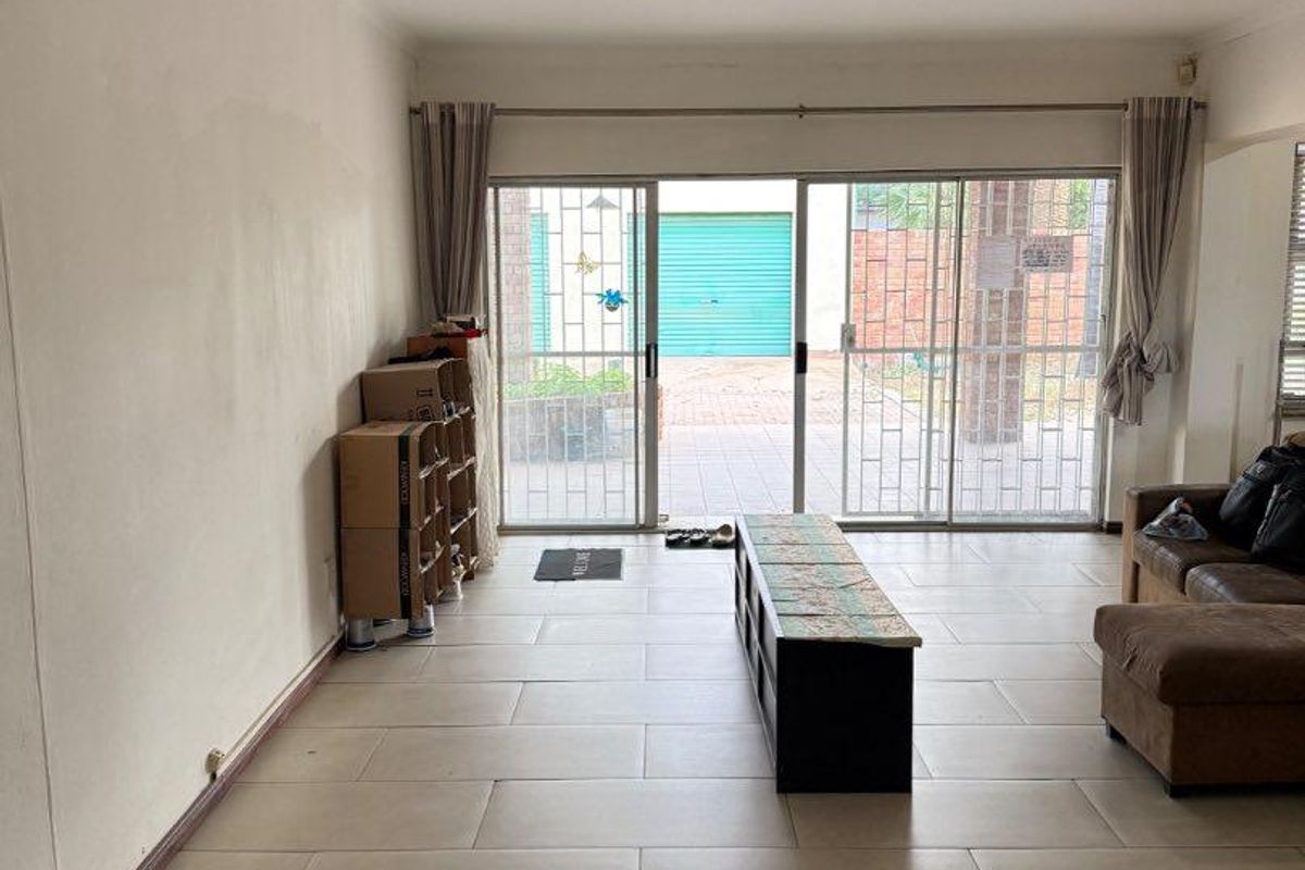 Spacious living area featuring large sliding glass doors with security gates, tiled flooring, and direct access to the outdoor patio area.