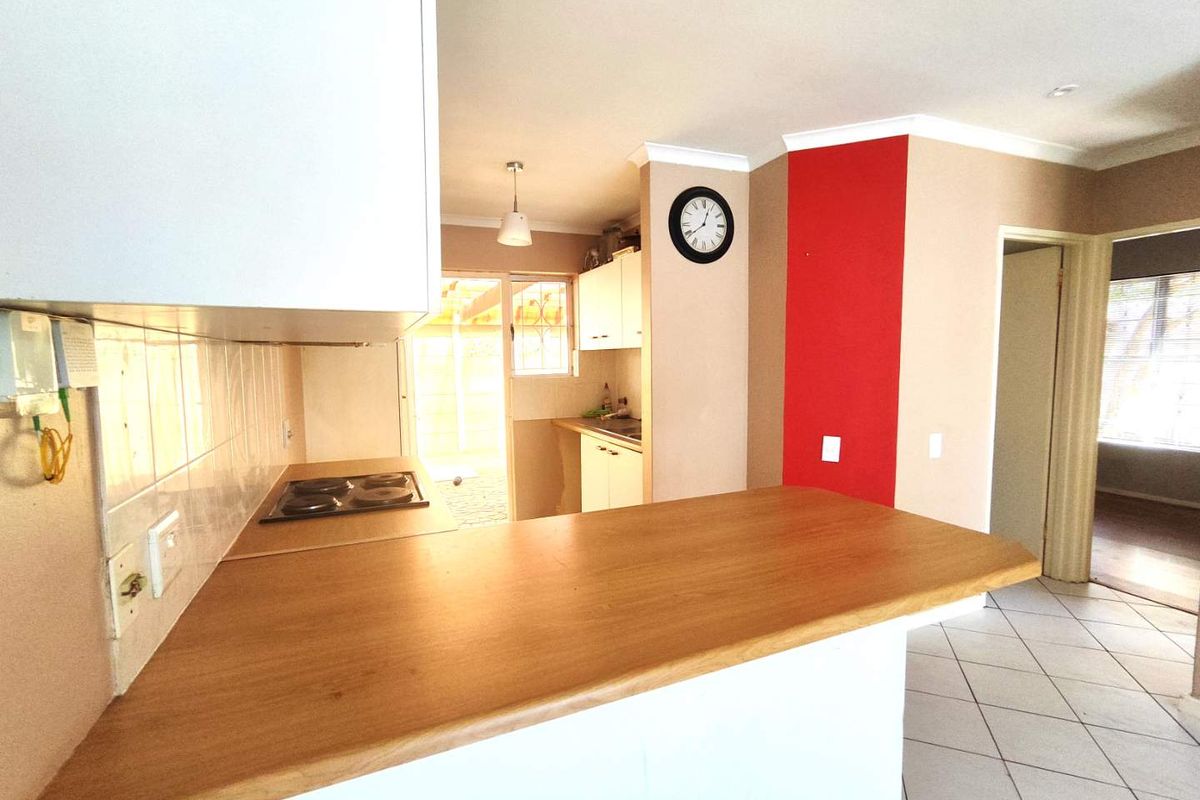 Functional kitchen featuring a breakfast bar, electric hob, tiled splashback, and built-in cabinetry with direct access to the rear outdoor area.